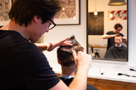 Barber is hairdressing the hair of a young man with a comb in his barbershop, ready to cut hair