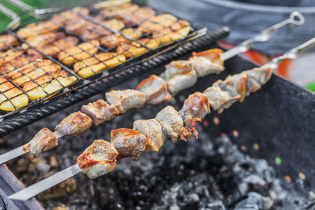 Pork shashlik with pieces of potatoes being roasted on skewers over charcoalの写真素材