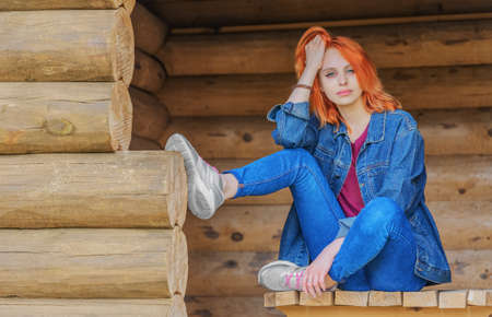 Beautiful young woman sitting at arbor and looking into the distance. Summer evening in villageの写真素材