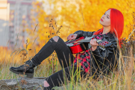 Beautiful young woman sitting with guitar. autumn dayの写真素材