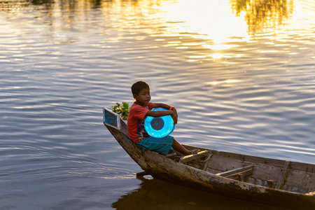 Tonle Sap, Cambodia - January 04, 2017: A young boy on a canoe carries a can of water in the Tonle Sap Lake at sunset. Tonle Sap is the largest freshwater lake in Southeast Asiaのeditorial素材