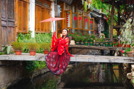 Lijiang, China - April 29, 2019: A fashion model with traditonal clothing and umbrella posing in Lijiang old town over a wooden pedonal bridgeのeditorial素材