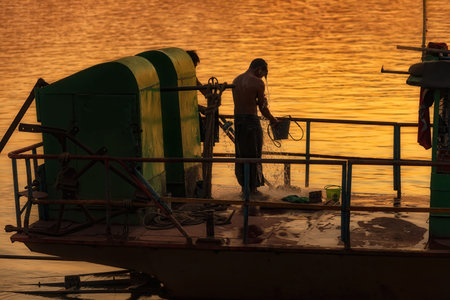 Monywa, Myanmar - December 22, 2019: View of a man taking a shower on his boat before going to home. Along the river coastline there are always a lot of movement of people at the end of working dayのeditorial素材
