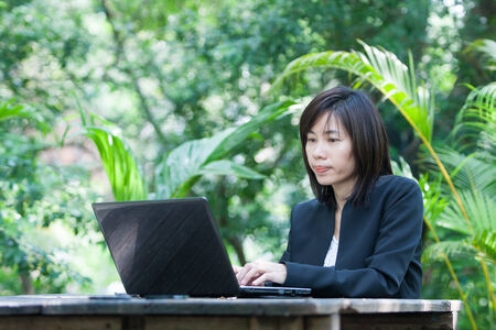Woman sitting use computer on wooden table at home office ,background of green trees.の写真素材