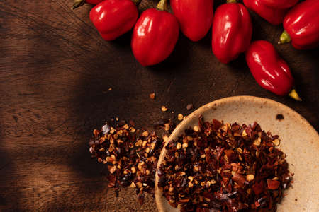 Assorted hot chilli pepper and crushed peppers on wooden surface with space for text.  Ideal for food recipe or restaurant menuの写真素材