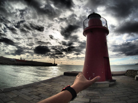 Hand taking lighthouse at dusk, harbour entrance of Castiglione della Pescaia, Maremma.