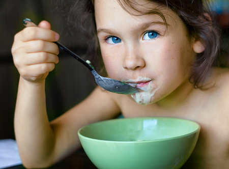 Portrait of a little girl 6 years eating healthy breakfast. Blue eyes.の写真素材