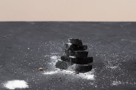 Fractured pieces of charcoal bread sprinkled with crumbs on black surface.