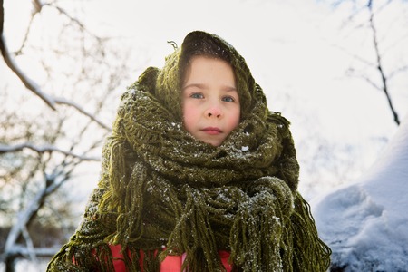Portrait of a cute girl wrapped in a big shawl on sky background. The girl looks at the camera.の写真素材