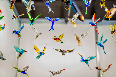 Lots of multi-colored glass birds hang from the ceiling on strings.の写真素材