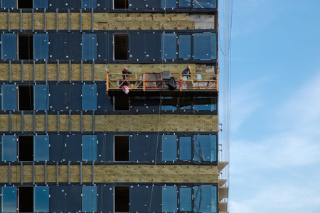 Facing the building with a ventilated facade and hoist with workers. Modern facades of high-rise...
