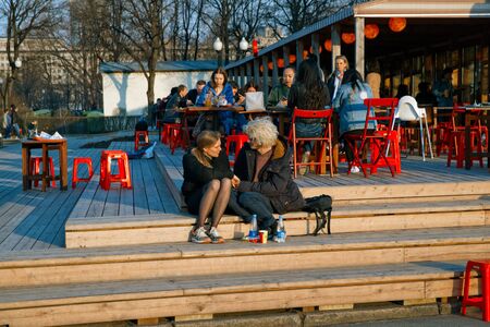 Russia, Moscow, April 15, 2018. A pair of lovers sit on steps of street cafe in spring at the end of day at sunset.のeditorial素材