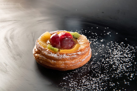 Bun sprinkled with powdered sugar, berries, grape, kiwi, orange