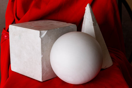 Cube, ball and cone mounted on a chair covered with beautiful red textilesの写真素材