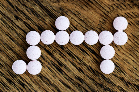 White pills in the form of a cross on a wooden background.の写真素材