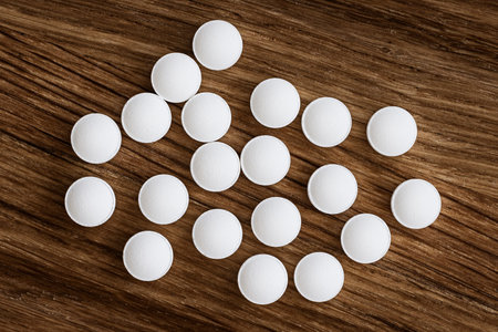 Heap of white pills on a wooden background. Top view.