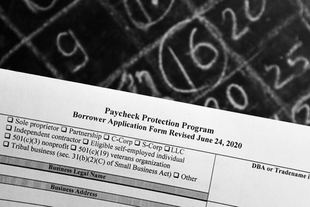 selective focus monochrome photo of paycheck protection program borrower application form revised, on a background of chalk board with numbersの写真素材