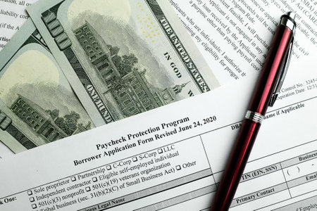 close-up of paycheck protection program borrower application form revised topview, on a background of dollar bills and a penの写真素材