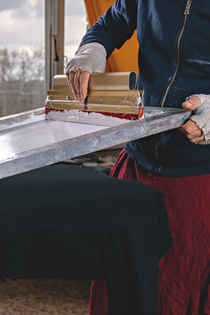 selective focus photo of male hands with squeegee. serigraphy production. printing images on t-shirts by silkscreen method in a design studioの写真素材