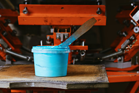 selective focus photo of can of blue paint on wooden shelve on the print screening apparatus. serigraphy production. printing images on t-shirts by silkscreen method in a design studioの写真素材