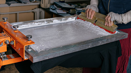 selective focus photo of male hands with squeegee. serigraphy production. printing images on t-shirts by silkscreen method in a design studioの写真素材