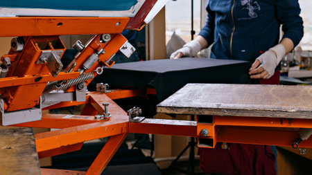 selective focus photo of print screening apparatus and worker. serigraphy production. printing images on t-shirts by silkscreen method in a design studioの写真素材