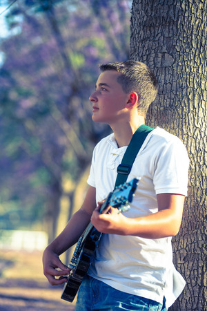 young musician with a guitar near a treeの写真素材