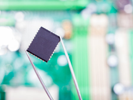 microchip in the tweezers on the background of the computer motherboard