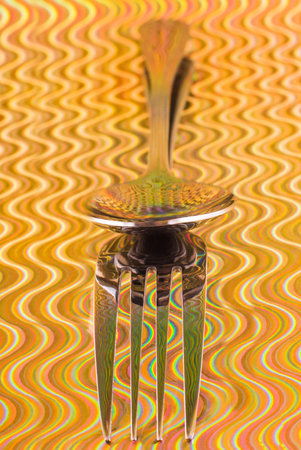 silver spoon and fork with reflection on a colored background