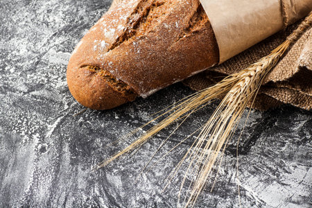 long loaf with ears of wheat on a dark background with flour