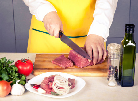 woman cuts meat fillet on a table with spices and vegetables