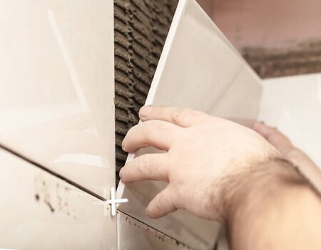 Worker tiler puts ceramic tiles on a wallの写真素材