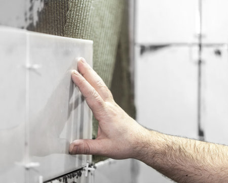 Worker tiler puts ceramic tiles on a wallの写真素材