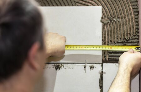 Worker tiler puts ceramic tiles on a wallの写真素材