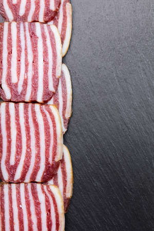 slices of sausage with bacon on dark backgroundの写真素材