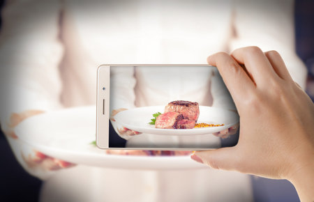 Hand with the phone close-up.woman photographs the cooked meat to a smartphone