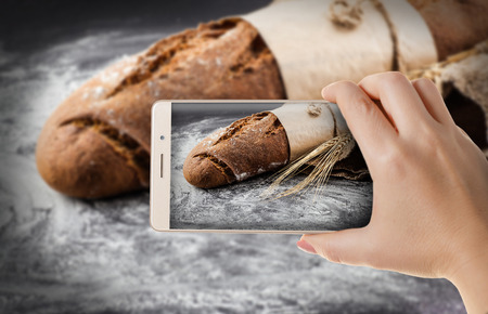 Hands with the phone close-up.Woman photographed fresh baked bread to a smartphoneの写真素材