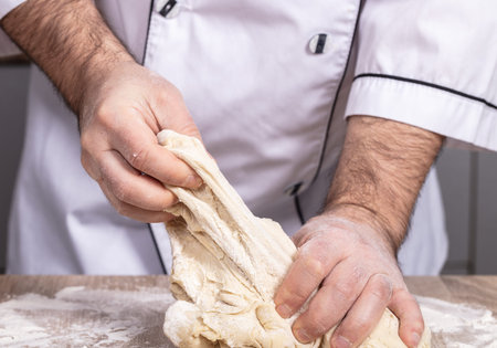 male cook kneads dough on the table, hands close-up