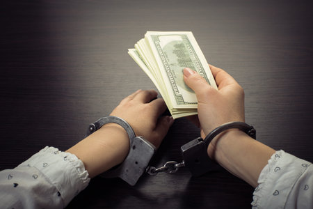 hands in handcuffs holding paper money on a wooden background