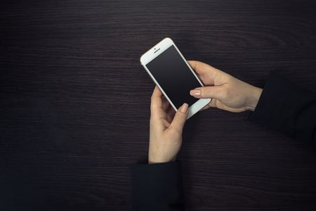 mobile phone in female hands on a wooden backgroundの写真素材