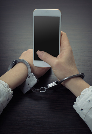 handcuffed hands with a mobile phone on wooden backgroundの写真素材