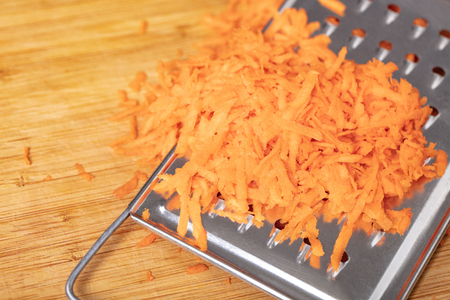 shredded carrots on a grater closeup, wooden backgroundの写真素材