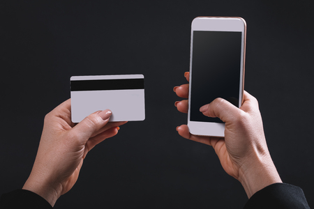 female hands hold mobile and bank card on black backgroundの写真素材