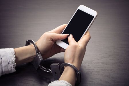 handcuffed hands with a mobile phone on wooden backgroundの写真素材