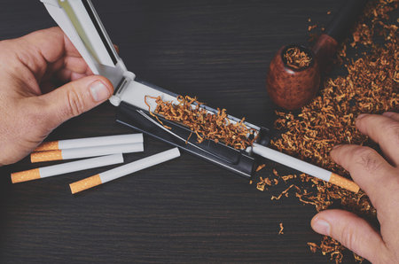 man makes a cigarette with rolling machine, hands closeup