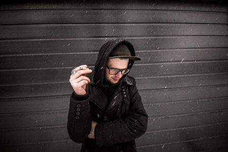 Smoking. a young man smoking a cigarette in black clothes on black texture background with snowの写真素材