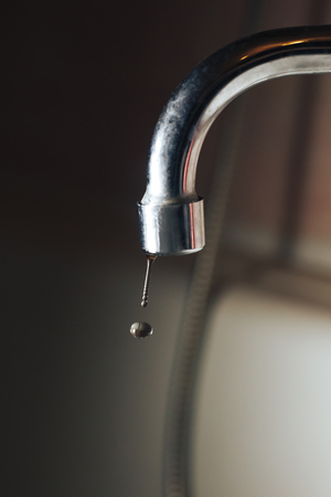 Metal faucet with falling drops of water close-upの写真素材
