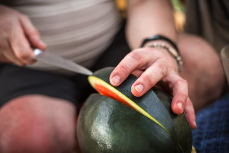 Men hand hold from on fresh watermelon cutting for eatin on table background. Male cutting a delicious sweet watermelonの写真素材