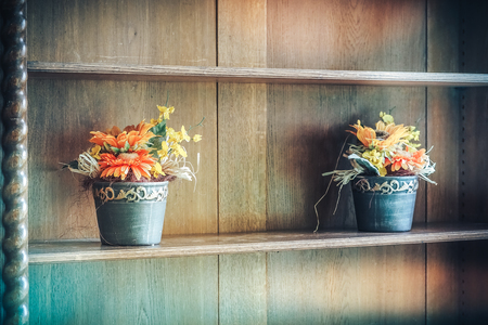 Artificial multi-colored flowers on the shelf in the closet, as the decor of the house and comfort, with sunlightの写真素材