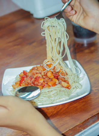Spaghetti with tomato sauce in a white plate being scooped with a fork.の写真素材